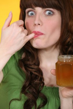 Woman dipping little finger in jar of honey clipart