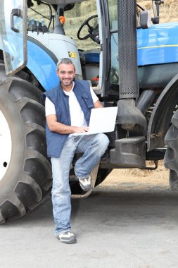 Famer with laptop computer stood by tractor clipart