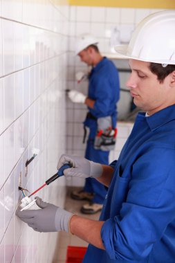 Pair of electricians wiring a white tiled room clipart