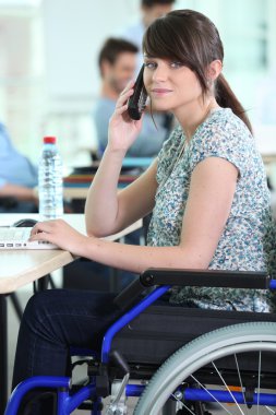 Young woman in a wheelchair at her desk clipart