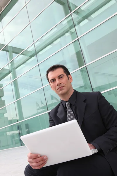 Businessman using a laptop outside a glass building — Stock Photo, Image