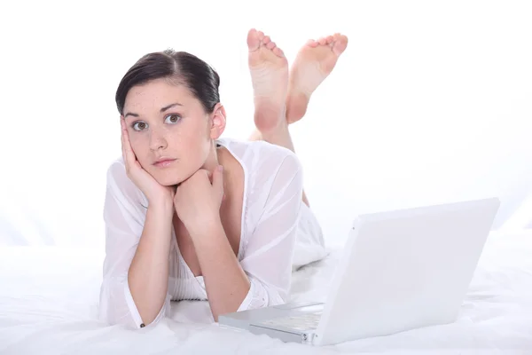 Jonge vrouw liggen op een bed in de buurt van een laptop — Stockfoto