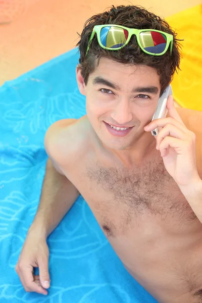 Bir cep telefonu ile sahilde yatan genç adam — Stok fotoğraf
