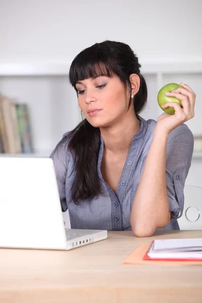 Mulher usando um laptop com uma maçã na mão — Fotografia de Stock