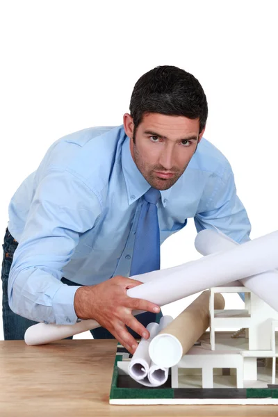 Молодой архитектор наклоняется над столом с чертежами и моделью — стоковое фото