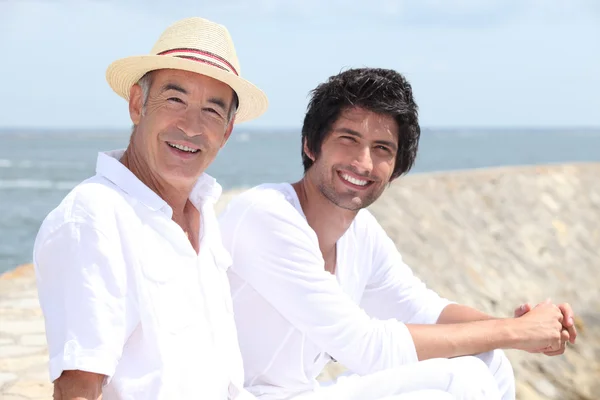 65-річний чоловік і 30-річний чоловік сидить на піску з фоном — стокове фото