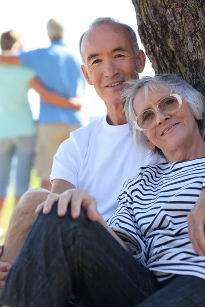 Pár důchodců pózuje sedící proti kmen — Stock fotografie
