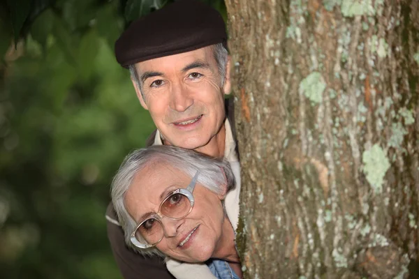 Пожилая пара за деревом — стоковое фото