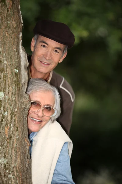 Starší pár, schovává se za strom — Stock fotografie