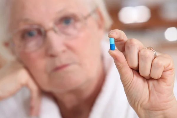 Elderly woman holding a capsule between her fingers — Stock Photo, Image