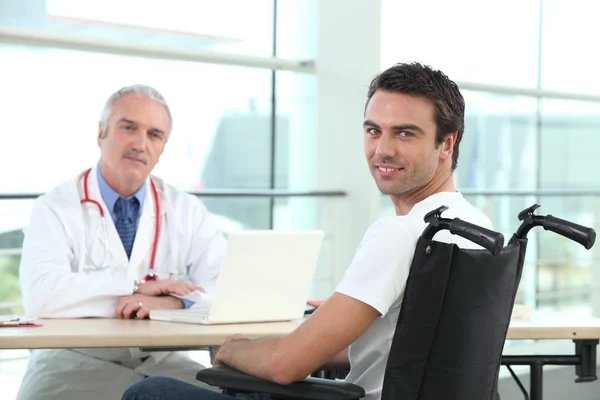 Молодий чоловік у інвалідному візку розмовляє з лікарем — стокове фото