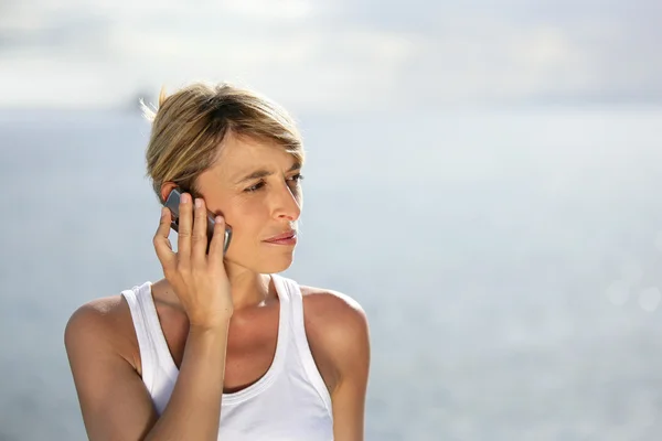 Blond woman making at call at the coast — Stock Photo, Image
