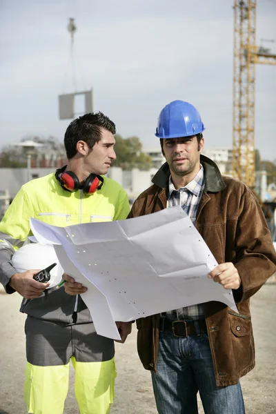 Trabalhadores da construção olhando para os planos do local — Fotografia de Stock