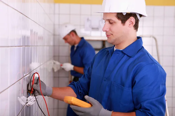 Two young electricians at work in a tiled room — Stock Photo, Image