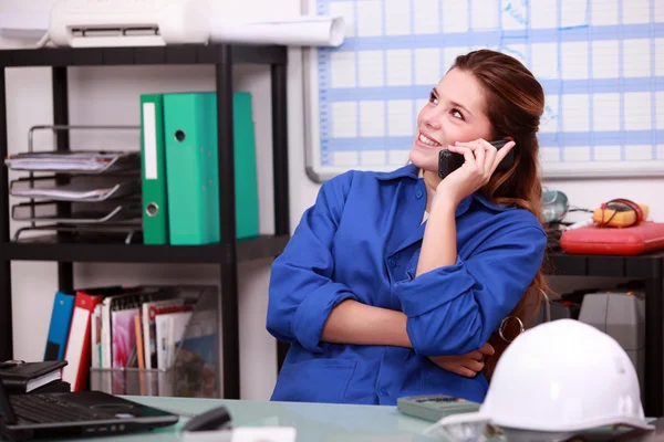 Junge Frau in blauem Overall am Telefon in einem Depot — Stockfoto