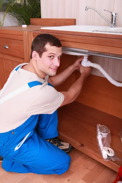 Un fontanero colocando un tubo flexible debajo de un grifo — Foto de Stock