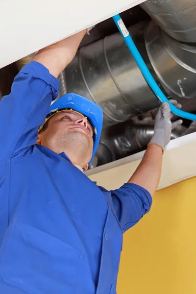 Fontanero sosteniendo un tubo flexible azul bajo algunos conductos de aire —  Fotos de Stock