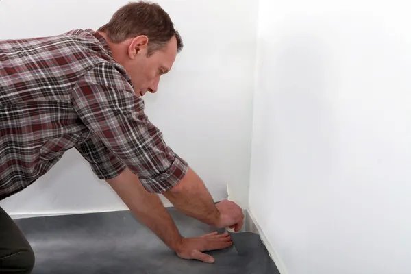 Man fitting linoleum flooring into the corner of a room — Stock Photo, Image