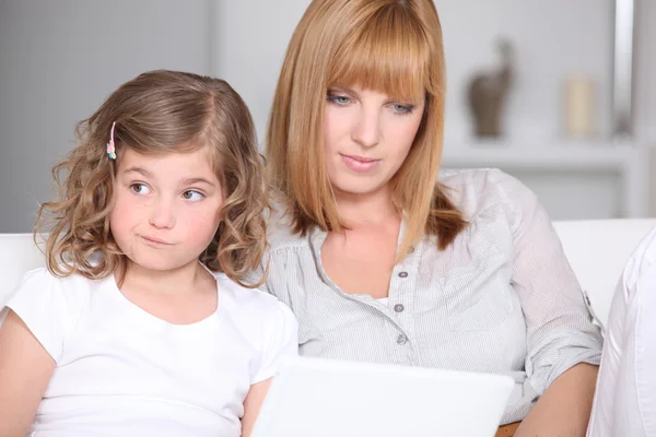Unimpressed little girl with her mother and a laptop — Stock Photo, Image