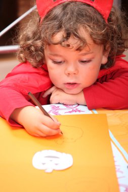 Closeup of a child in a red devil's outfit drawing jack-o-lanterns clipart