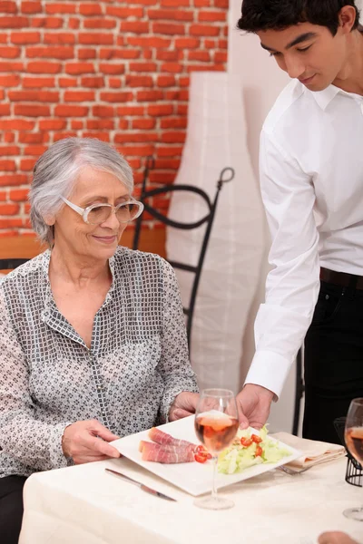 Young waiter serving lunch to an older customer — Stock Photo, Image