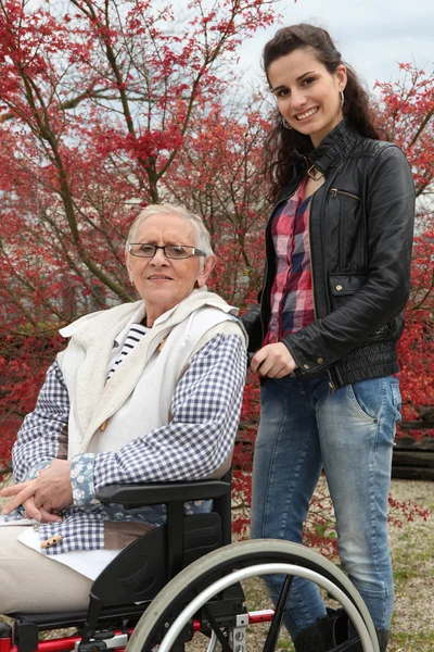 Młoda kobieta pchanie starsza pani na wózku inwalidzkim — Zdjęcie stockowe