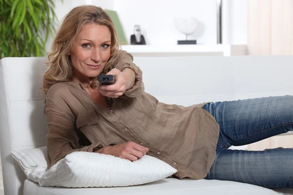 Mujer acostada en el sofá sosteniendo la televisión de control remoto —  Fotos de Stock