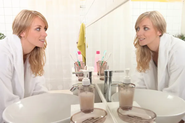 Ung kvinna som tittar på sin spegelbild i en badrumsspegel — Stockfoto