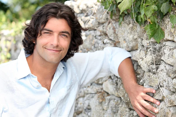 Stock image Good looking man leaning against an old stone country wall