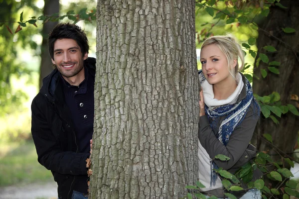 Un giovane uomo vestito di cappotto e una giovane donna bionda in posa vicino ad un albero — Foto Stock