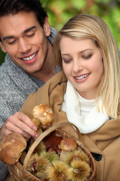 Jovem casal com cesta cheia de cogumelos e castanhas — Fotografia de Stock
