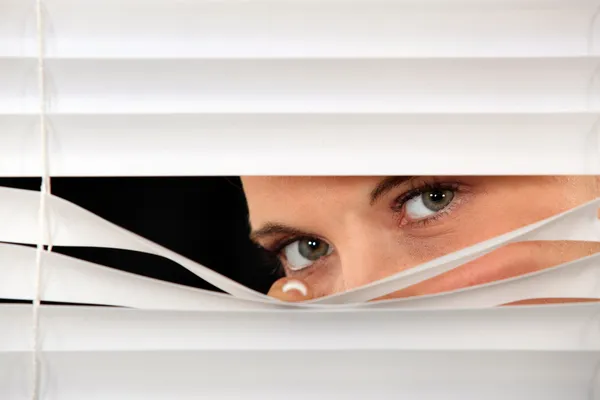 Mulher espreitando através de cortinas venezianas — Fotografia de Stock