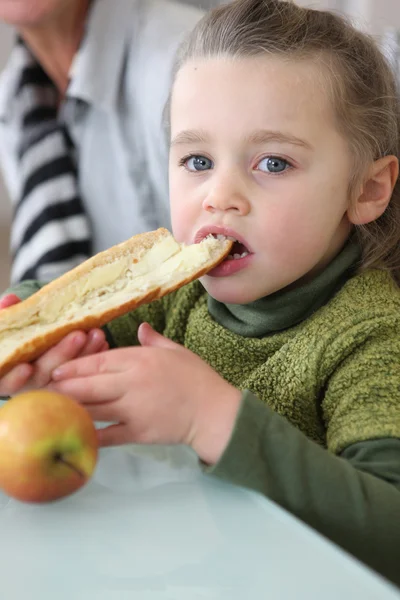 Girl eating slice of buttered bread — Stock Photo, Image