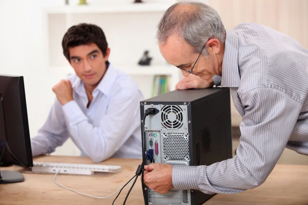 Gammal man pluggar en dator under klockan av en ung man — Stockfoto