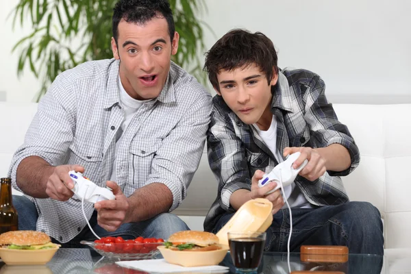 Vater und Sohn spielen Computerspiele und essen Junk Food — Stockfoto