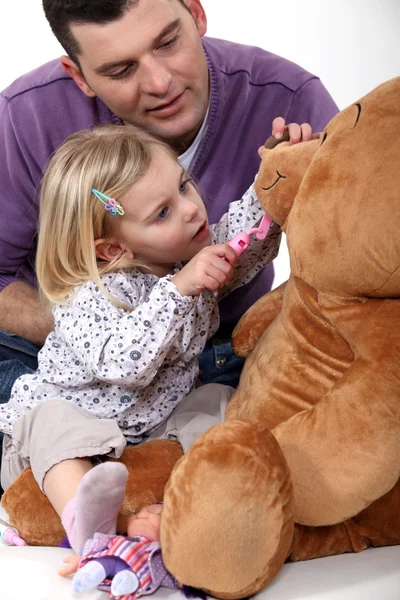 Отец и дочь играют в дантиста с плюшевым мишкой — стоковое фото
