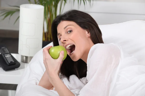 Mujer mordiendo una manzana verde en la cama —  Fotos de Stock