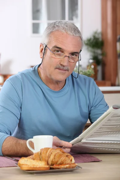 Muž středního věku, čtení novin, zatímco jíst snídani — Stock fotografie