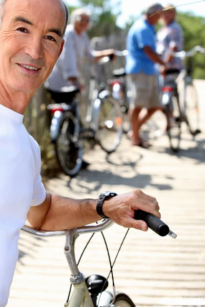 Uomo anziano con una bicicletta e i suoi amici sullo sfondo — Foto Stock