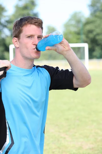 Man stood by soccer pitch drinking energy drink — Stock Photo, Image