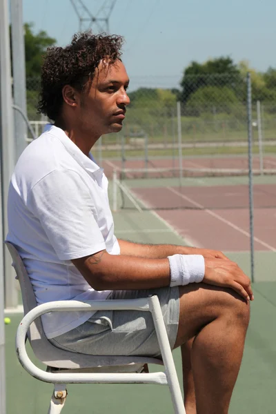 Теннисист сидит рядом с теннисным кортом — стоковое фото