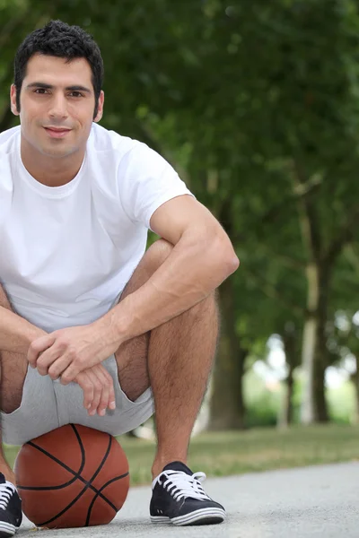 Man crouching on basketball — Stock Photo, Image