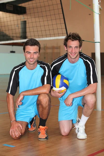 Члены команды стоят на коленях с волейбольным мячом на крытой площадке — стоковое фото