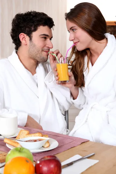 Молодая пара в халате пьет апельсиновый сок из соломы — стоковое фото
