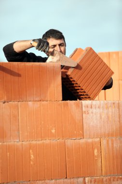 Bricklayer in construction site erecting red brick wall clipart