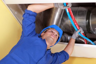 Worker holding blue and red pipes under air ducts clipart