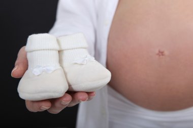 Pregnant woman holding her unborn baby's slippers clipart