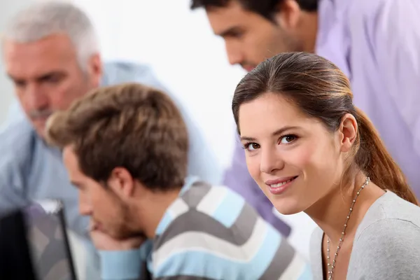 Smiling young woman with male colleagues out of focus in the background — Stock Photo, Image