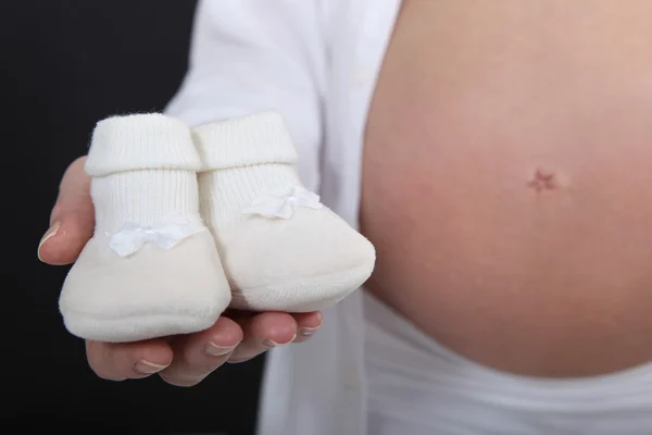 Mulher grávida segurando chinelos de seu bebê por nascer — Fotografia de Stock