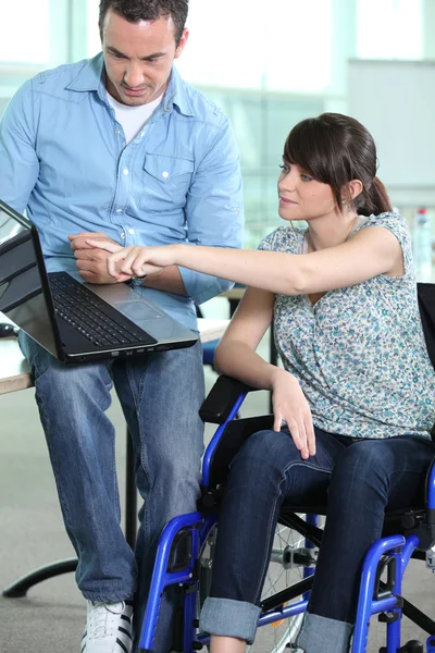 Mujer joven en silla de ruedas que se muestra algo en un ordenador portátil — Foto de Stock